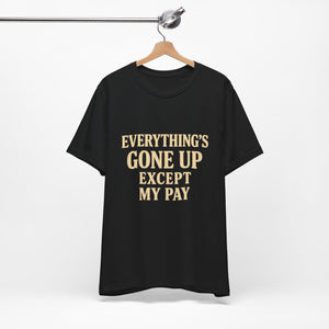 The "Everything's Gone Up Except My Pay" T-Shirt by Printify (Old Man Snark) features bold beige lettering on black Airlume cotton, displayed on a wooden hanger against a white background.