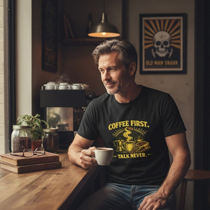 Old Man Snark black cotton t-shirt with yellow text "COFFEE FIRST. TALK NEVER." and coffee-themed graphics.