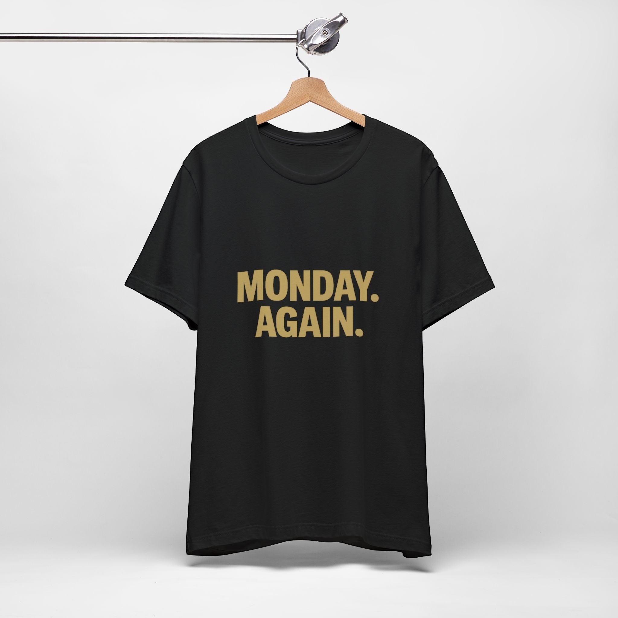 The "Monday. Again." T-Shirt by Old Man Snark (Printify) in black Airlume cotton hangs on a wooden hanger against a white background, with bold tan lettering—perfect for starting your week with motivation.