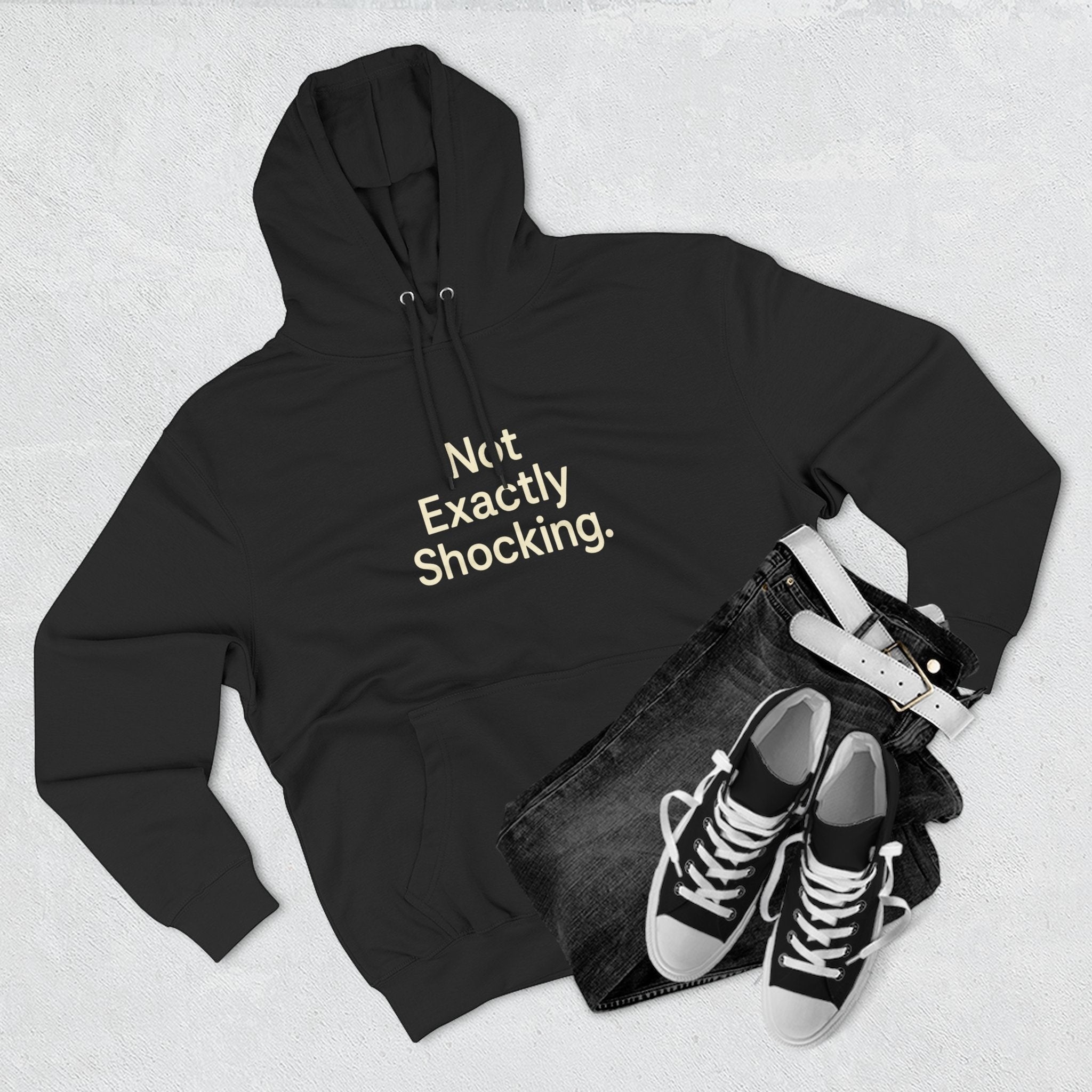 Old Man Snark black cotton-blend fleece hoodie with "Not Exactly Shocking." graphic in cream text on chest. Paired with dark wash jeans and white belt.