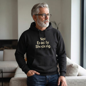 Old Man Snark black midweight fleece hoodie with Not Exactly Shocking slogan worn by a mature man with grey hair.