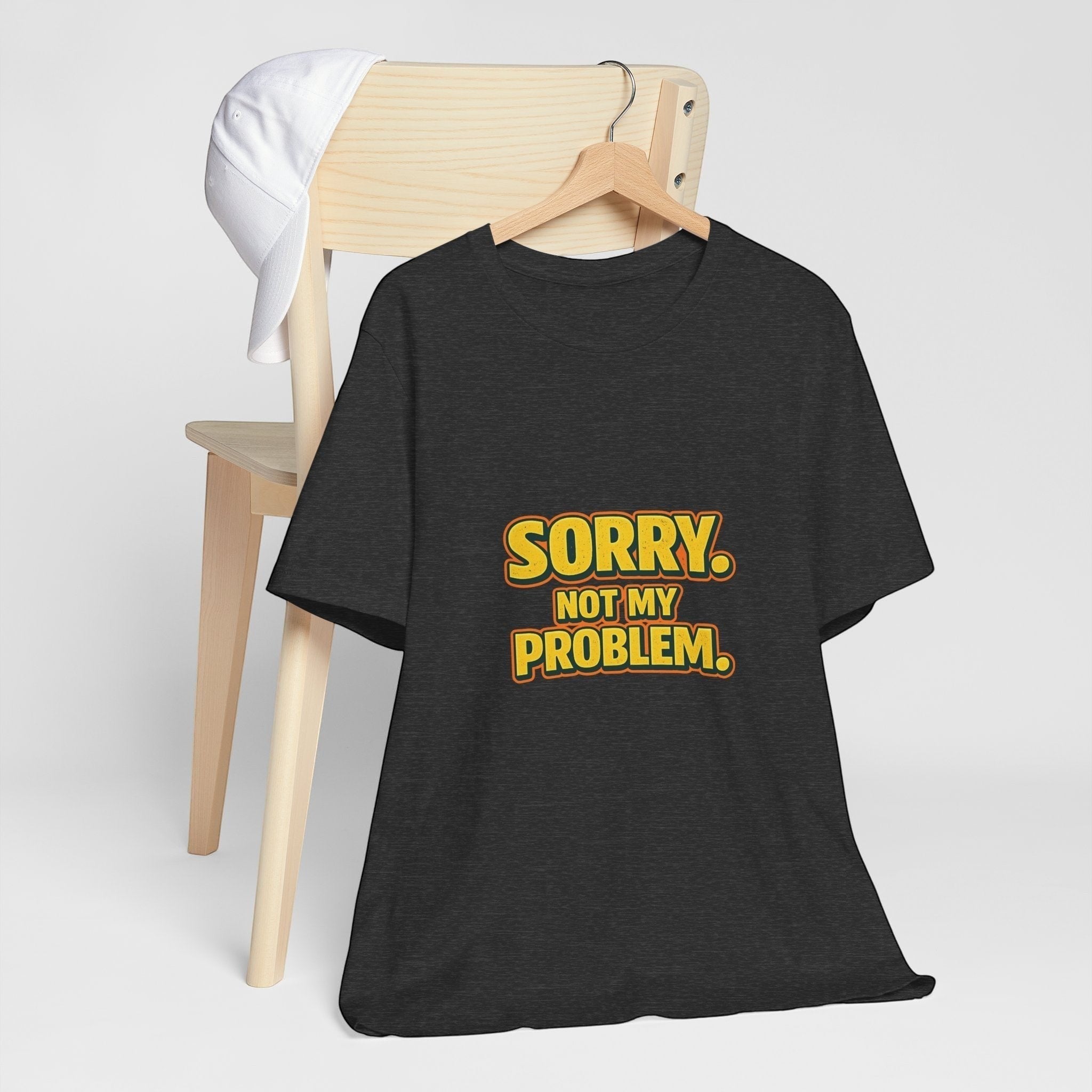 Old Man Snark black cotton t-shirt with retro gold and orange Sorry Not My Problem graphic on a wooden chair