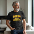 Old Man Snark black cotton t-shirt with retro gold and orange Sorry. Not My Problem. text worn by a bearded man.
