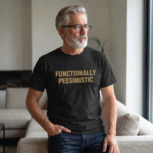 A gray-haired, bearded man with glasses sits on a beige couch in a modern living room, wearing the Printify "Functionally Pessimistic" T-Shirt by Old Man Snark.