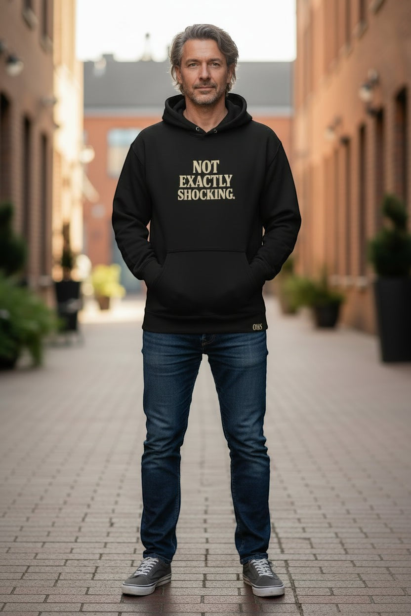 Old Man Snark black cotton-blend hoodie with "NOT EXACTLY SHOCKING." graphic in gold text on chest. Model wears size M.